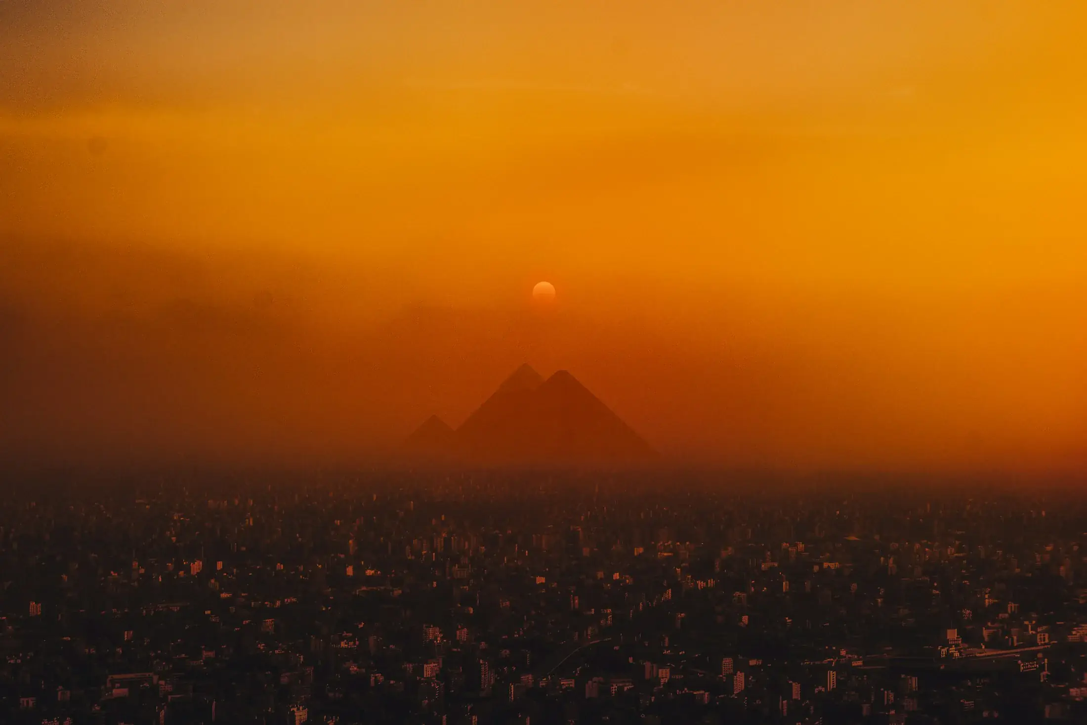The Giza pyramids silhouetted in orange light above the city